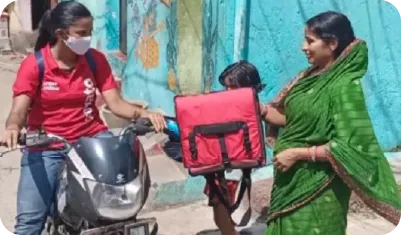 Volunteer distributing cooked food to children from large containers in a street feeding drive 